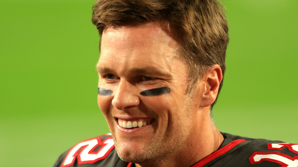 Tom Brady smiling and wearing eye black on a football field
