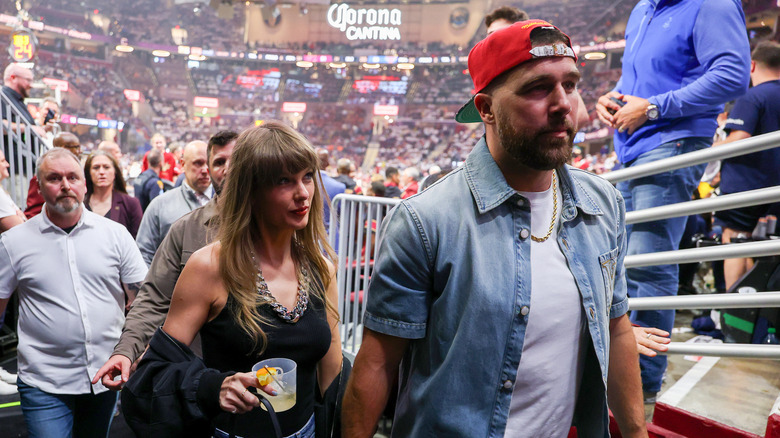 Taylor Swift looking at Travis Kelce as they walk together while holding hands