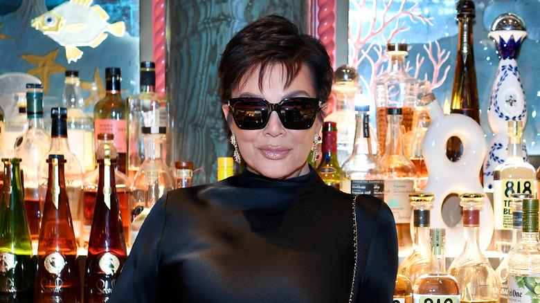 Kris Jenner smiling in sunglasses in front of bar