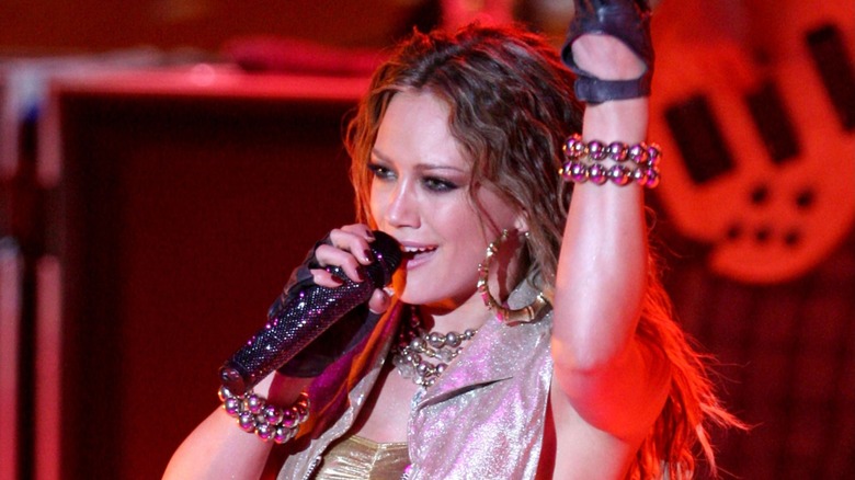 Dressed in a shimmery costume and pearly jewelry, Hilary Duff sings into a microphone