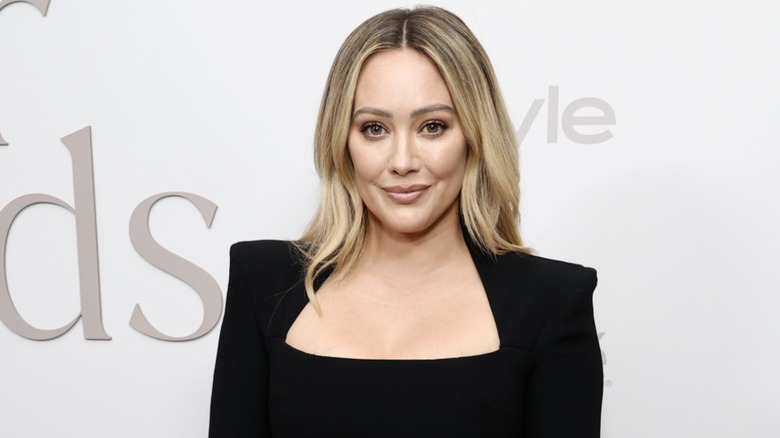 Hilary Duff looks directly into the camera while wearing a black suit with sharp shoulders