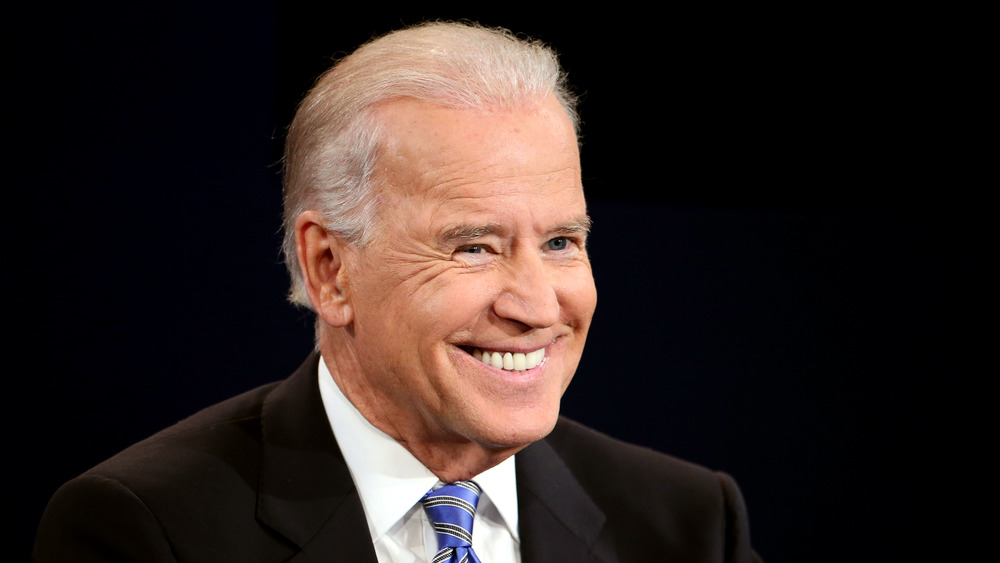 Joe Biden smiles on stage while wearing a suit and blue tie