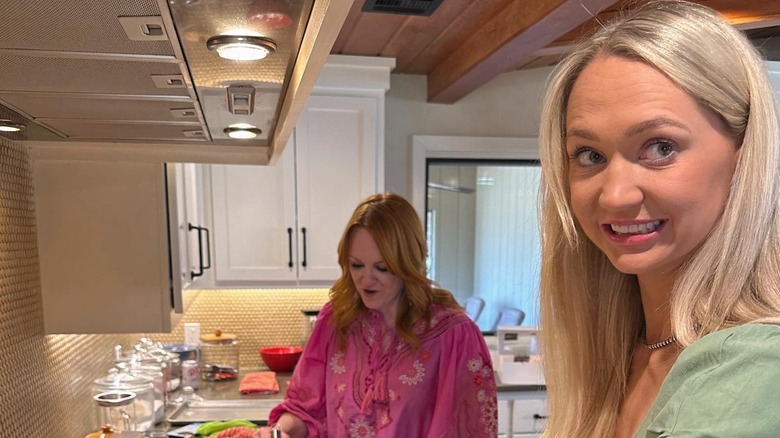 Paige Drummond grins as Ree Drummond gazes down while preparing a dish.