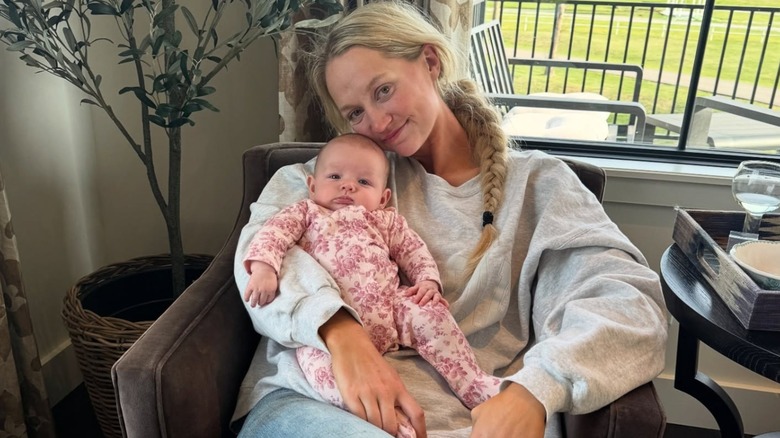 Wearing a loose sweatshirt, Paige Drummond tilts her head to the side and smiles gently while holding Baby Sofia.