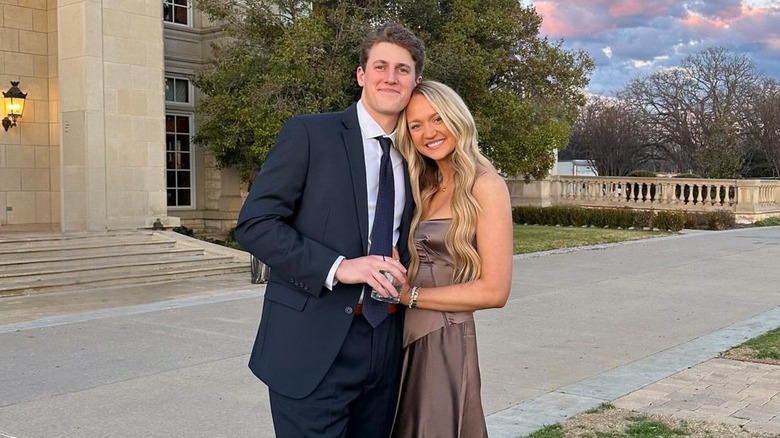 Standing close to each other while smiling gently, Paige Drummond and David Andersen hold hands.