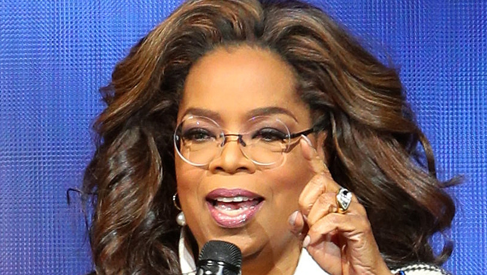 Oprah Winfrey talking into a microphone wearing glasses