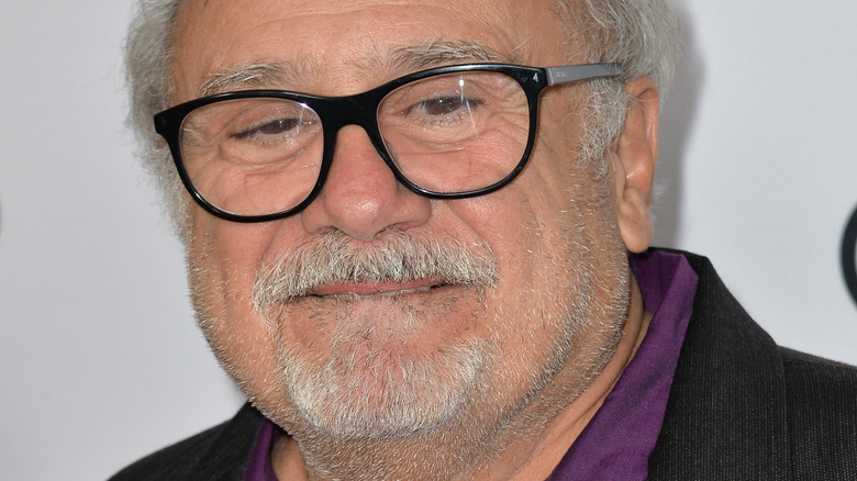 Danny DeVito poses in purple shirt and black glasses