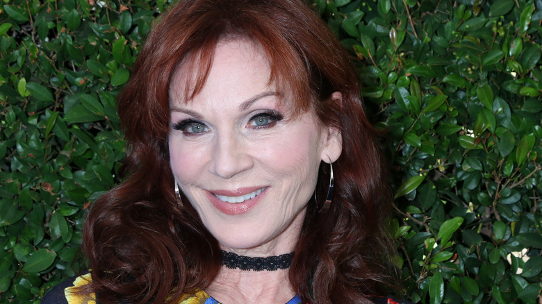 Marilu Henner wears eyeliner and a black choker in front of leaves