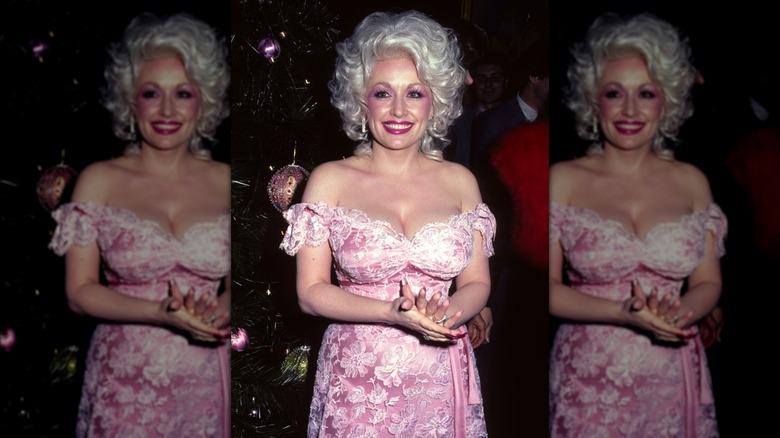 Dolly Parton smiling while posing in a pink off the shoulder dress