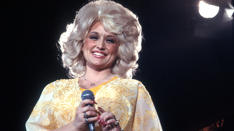 Dolly Parton smiling onstage in a flashy yellow outfit
