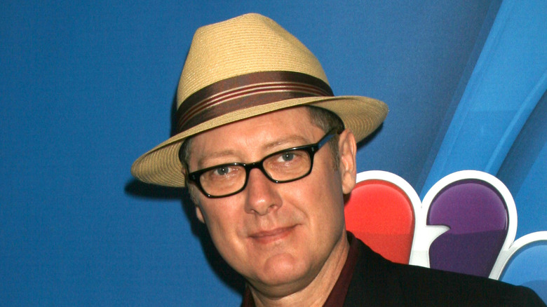 James Spader smiling in glasses and a hat