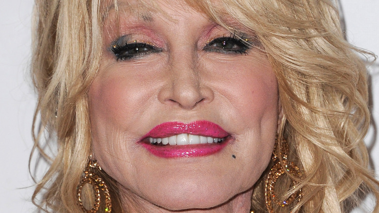 Dolly Parton wears hot pink lip gloss and gold earrings