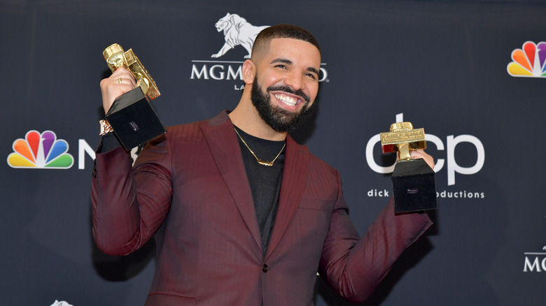 Drake with wide smile holding two music awards
