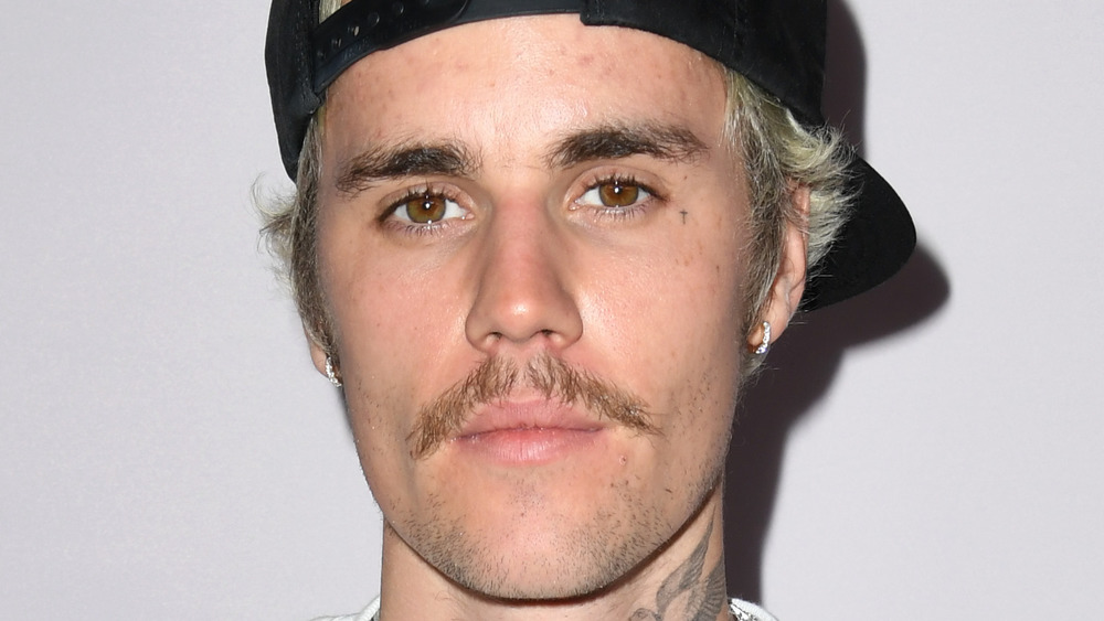 Justin Bieber sporting a mustache, backwards hat, and a serious look