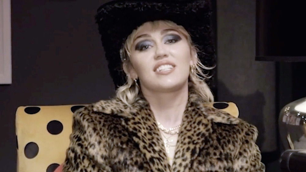 Miley Cyrus sits talking in a chair next to a guitar