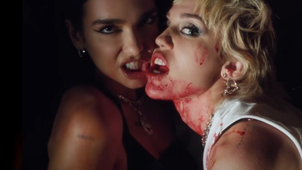 Dua Lipa and Miley Cyrus looking up and singing into microphones