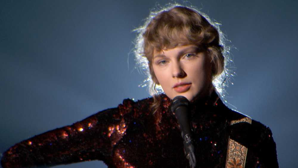 Taylor Swift holding a guitar in front of a microphone