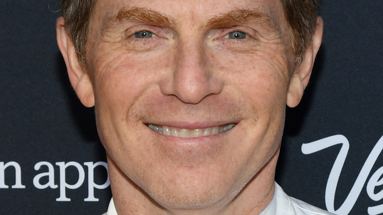 Bobby Flay smiles in a white chef coat