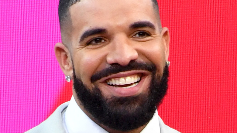 Drake in a grey suit against a pink background