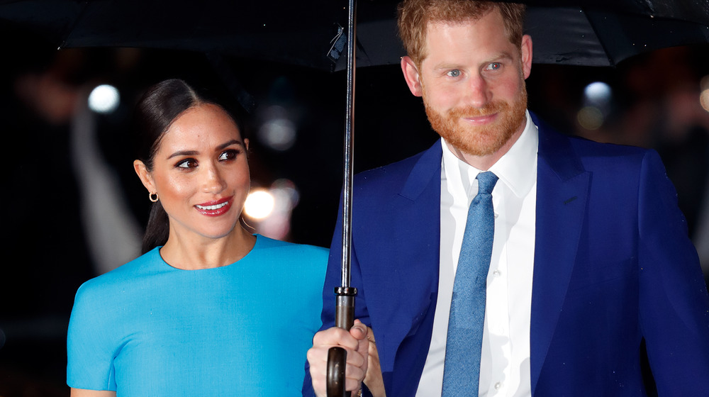 Meghan Markle and Prince Harry stands under an umbrella at an event