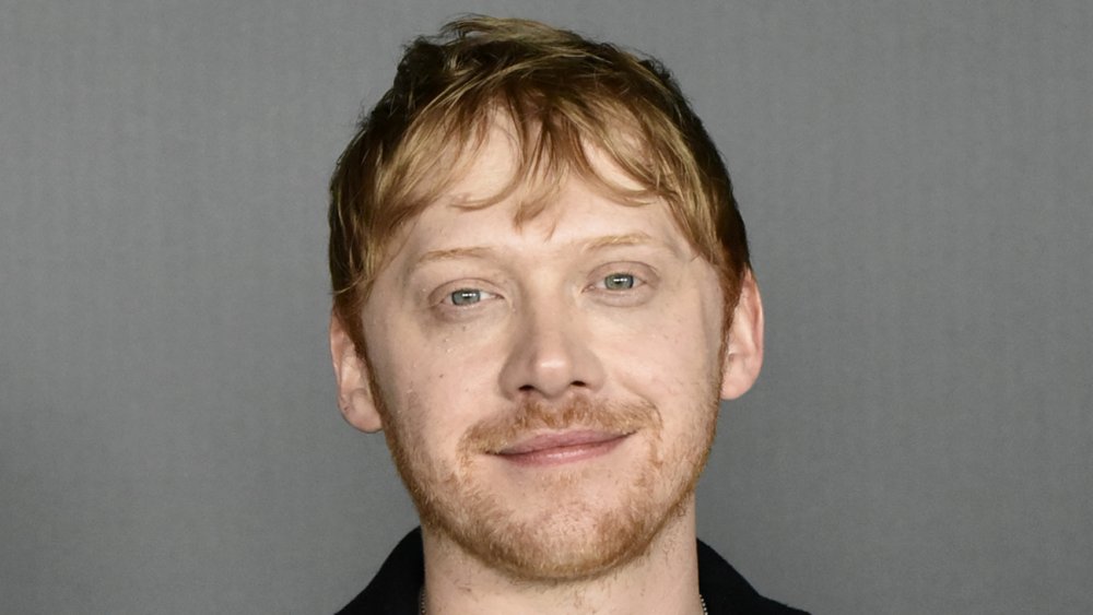 Rupert Grint wearing a black blazer, with a small smile, at an event