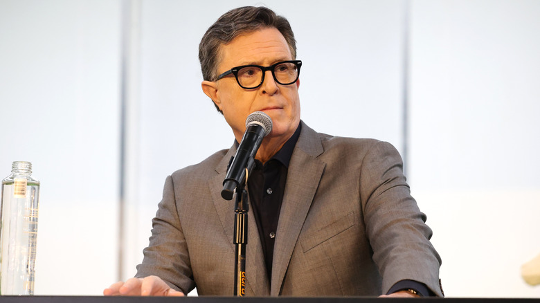 Stephen Colbert in a brown suit at a microphone