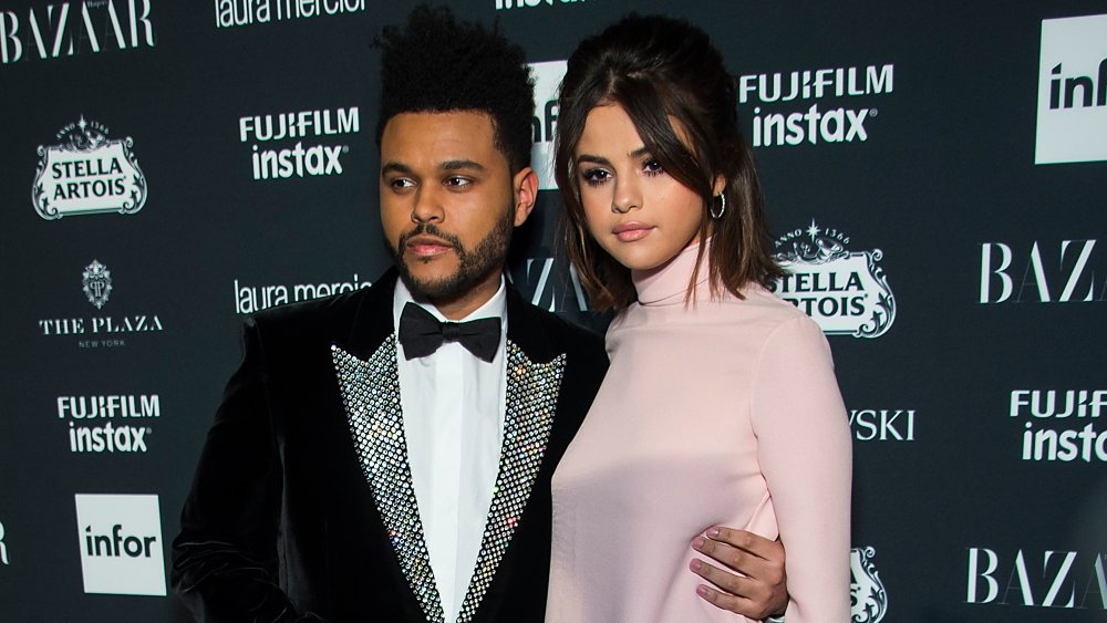 The Weeknd in a black velvet suit and bow tie, Selena Gomez in a pink dress, posing together on the red carpet