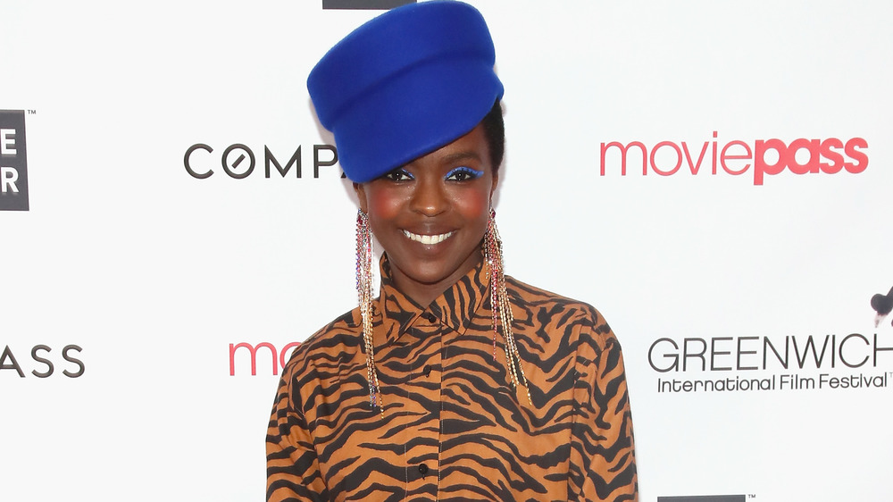 Lauryn Hill smiling in blue hat and tiger print blouse