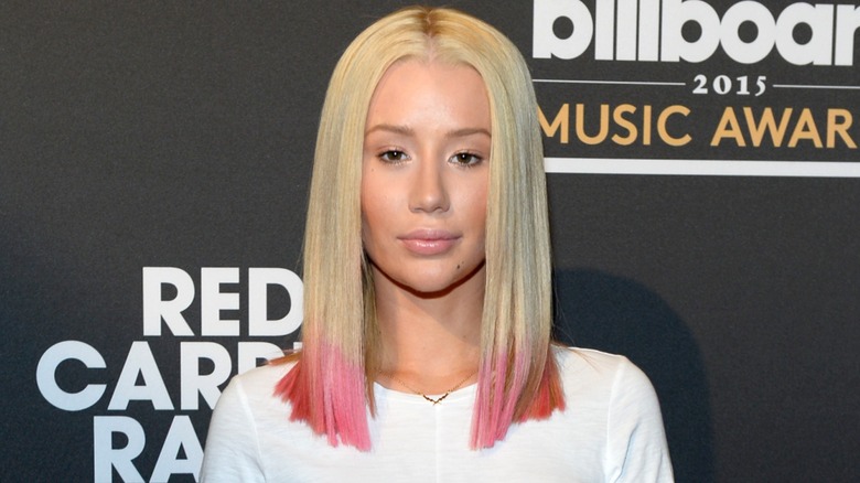 Sporting a blonde and pink hairdo and a white shirt, Iggy Azalea looks at the camera.