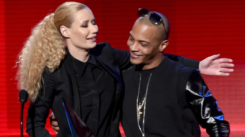 Rapper T.I. smiles and wraps his arms around Iggy Azalea's waist while she wraps one arm around his shoulders.