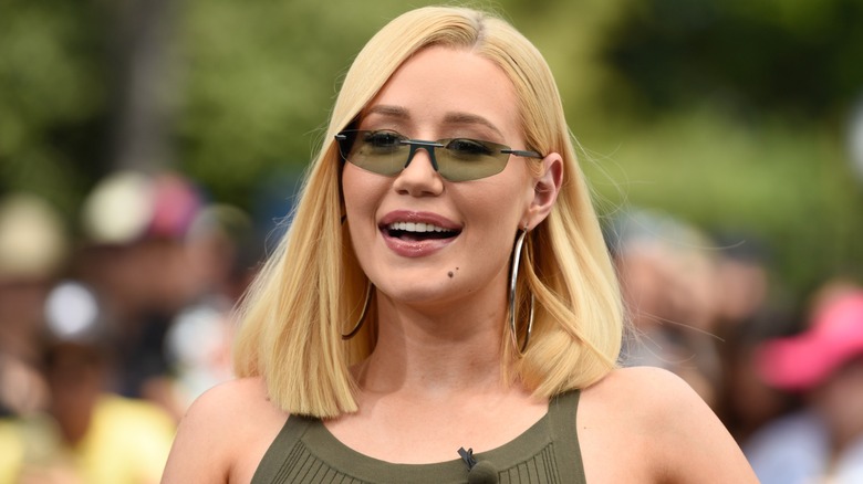 Iggy Azalea talks as she looks down, all while wearing a jungle green dress and matching sunglasses.