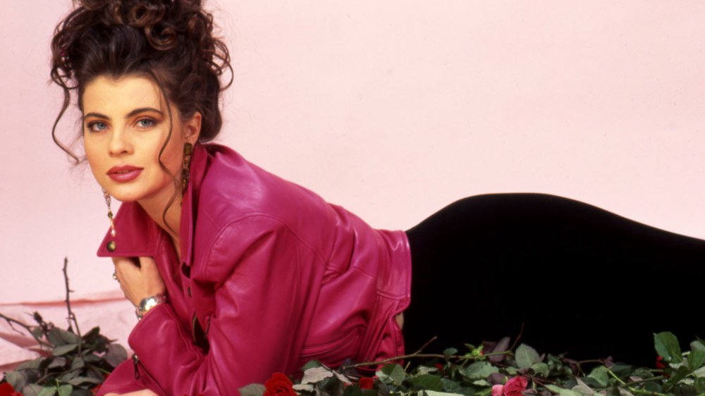 Yasmine Bleeth in a magenta leather jacket and black skirt, lying on a pile of roses during a photo shoot
