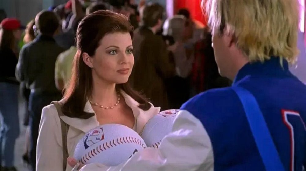 Yasmine Bleeth in Baseketball, wearing a khaki-colored blazer and gold necklace, with her hair pulled back in a half-ponytail 