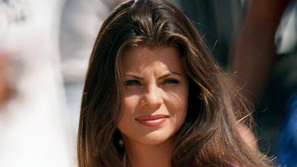Yasmine Bleeth in a purple top and gold heart necklace, glaring against the sun