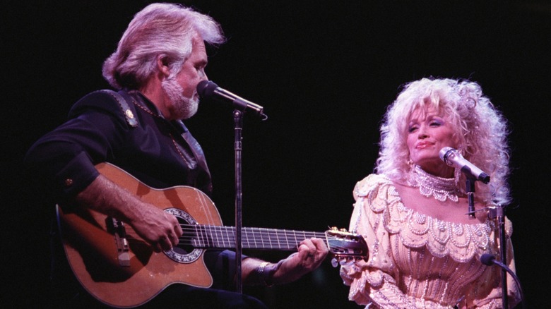 Kenny Rogers plays the guitar as Dolly Parton looks on.