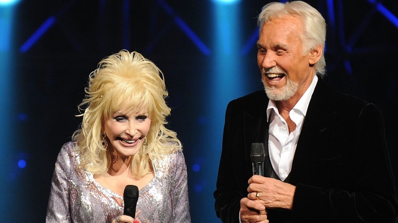 Dolly Parton and Kenny Rogers share a hearty laugh while holding microphones.