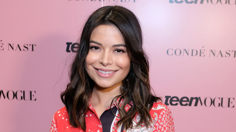 Miranda Cosgrove in a red, white, and black button up, smiling at a Teen Vogue event