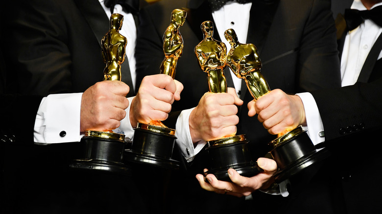 four men hold four Oscars