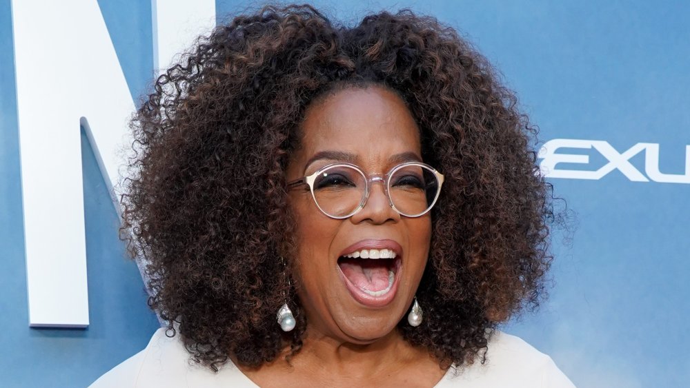 Oprah Winfrey in a white outfit, laughing on the red carpet