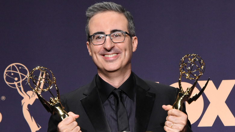 John Oliver smiling, holding Emmys
