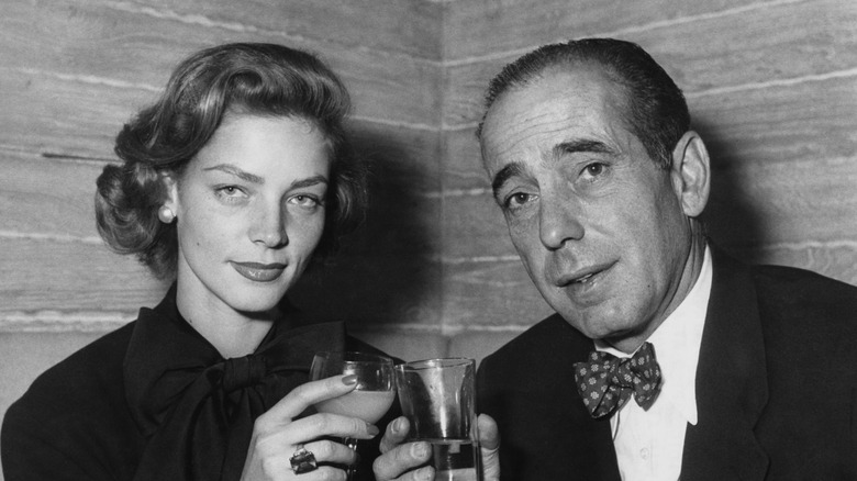 Lauren Bacall and Humphrey Bogart holding up drinks while attending a cocktail party in Paris
