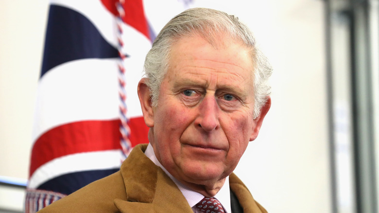 King Charles III looking serious in front of British flag