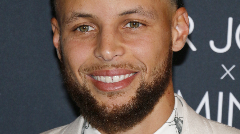 Steph Curry smiles in a tan suit