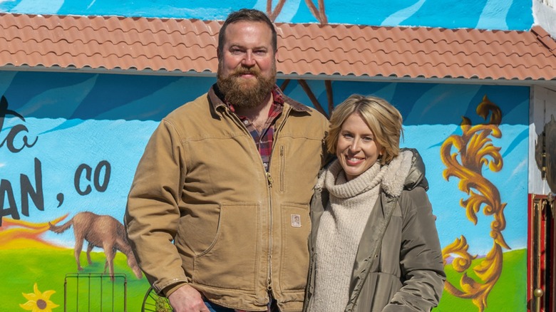 Ben and Erin Napier smiling in front of mural of blue sky