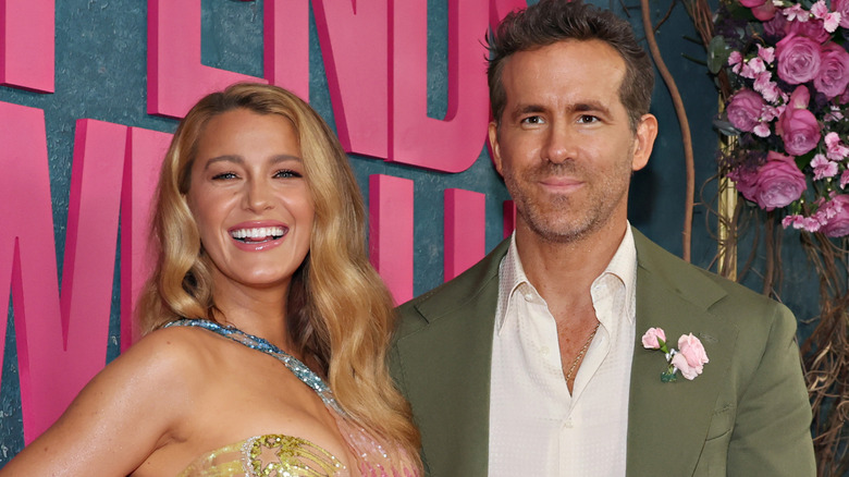 Blake Lively wearing an asymmetrical pastel gown and Ryan Reynolds wearing an olive green suit with a flower lapel and a white button down shirt on red carpet