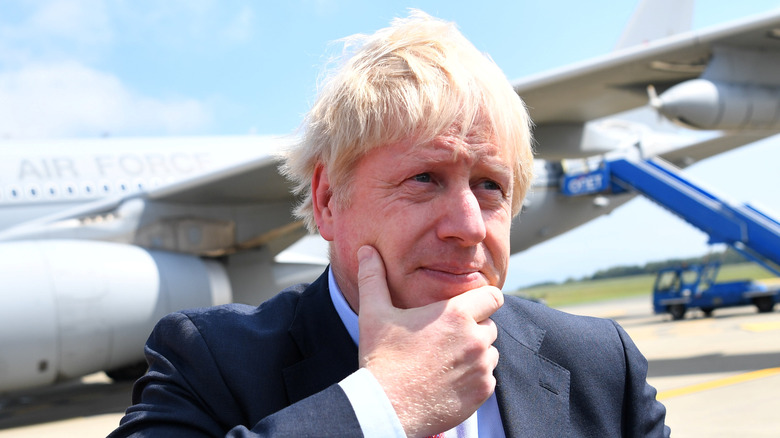 Boris Johnson in front of airplane, hand to chin