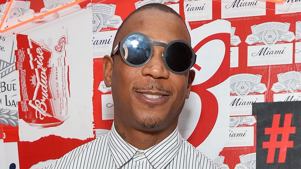 Ja Rule smiling in a white-and-black, pin-striped, button-up shirt and round, black-rimmed sunglasses