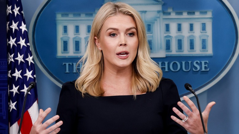 Dressed in black, Karoline Leavitt speaks with hand gestures at the White House briefing room.