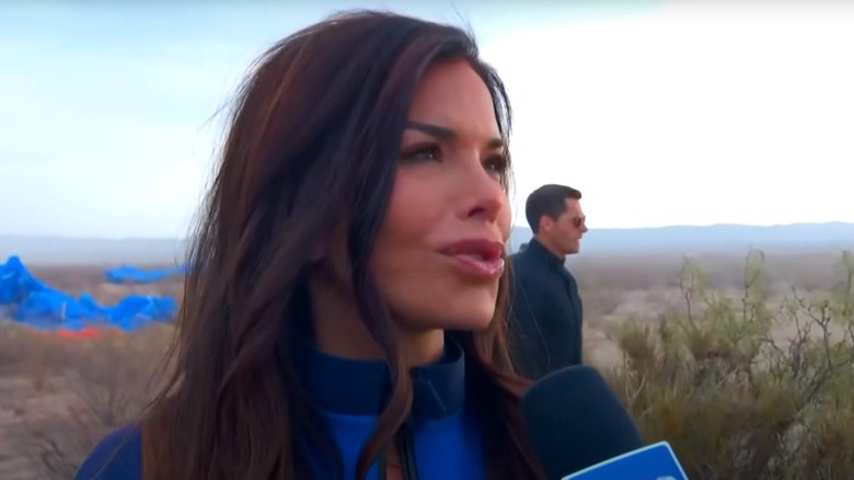Lauren Sanchez speaks into a microphone against a desert-like background.