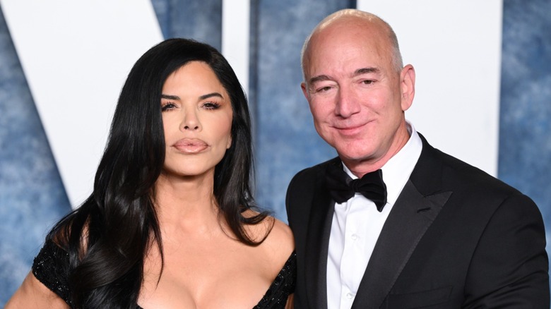 Lauren Sanchez pouts her lips as she fiercely stares at the camera while Jeff Bezos smiles subtly as he looks away.